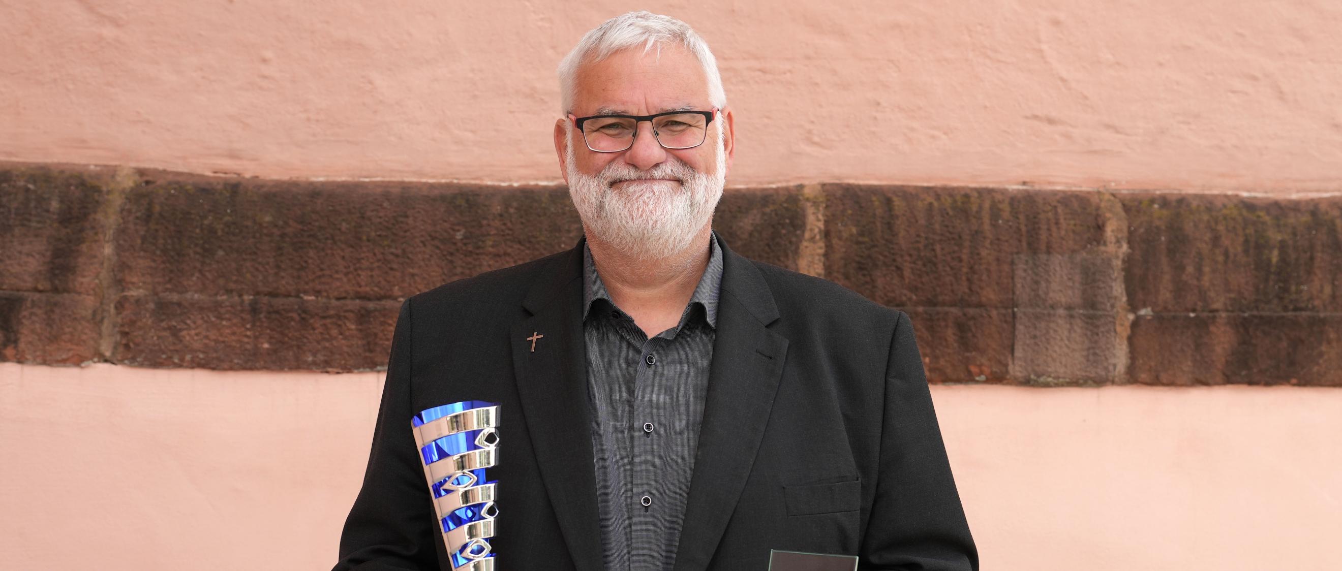 Ein lächelnder Mann hält zwei Pokale in den Händen