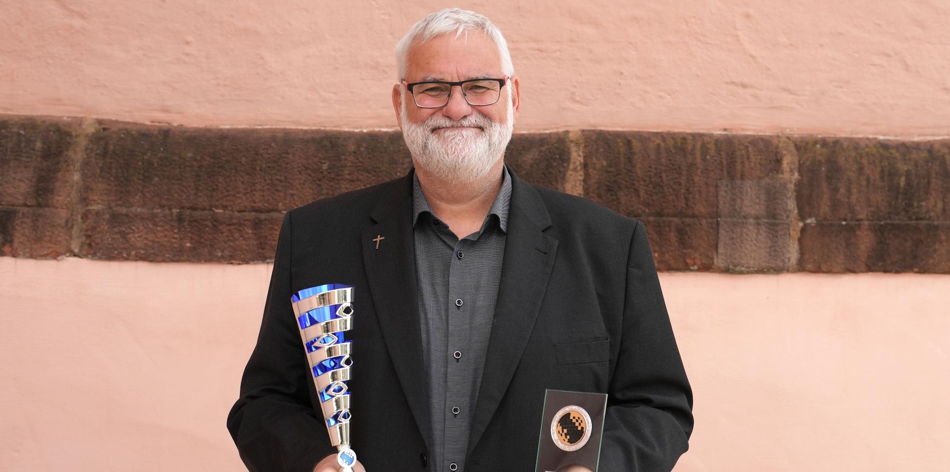 Ein lächelnder Mann hält zwei Pokale in den Händen