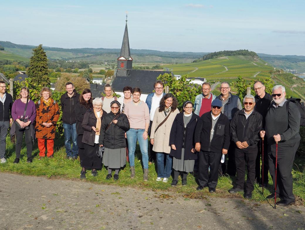 Eine Gruppe Menschen lacht vor einem Panorama mit einer Kirche in die Kamera
