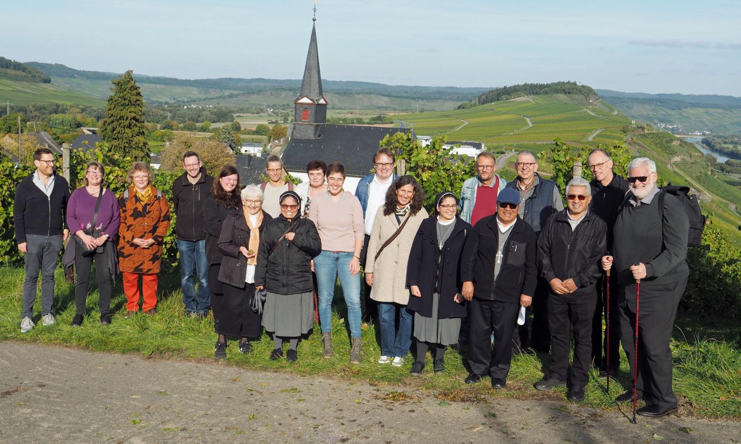 Eine Gruppe Menschen lacht vor einem Panorama mit einer Kirche in die Kamera