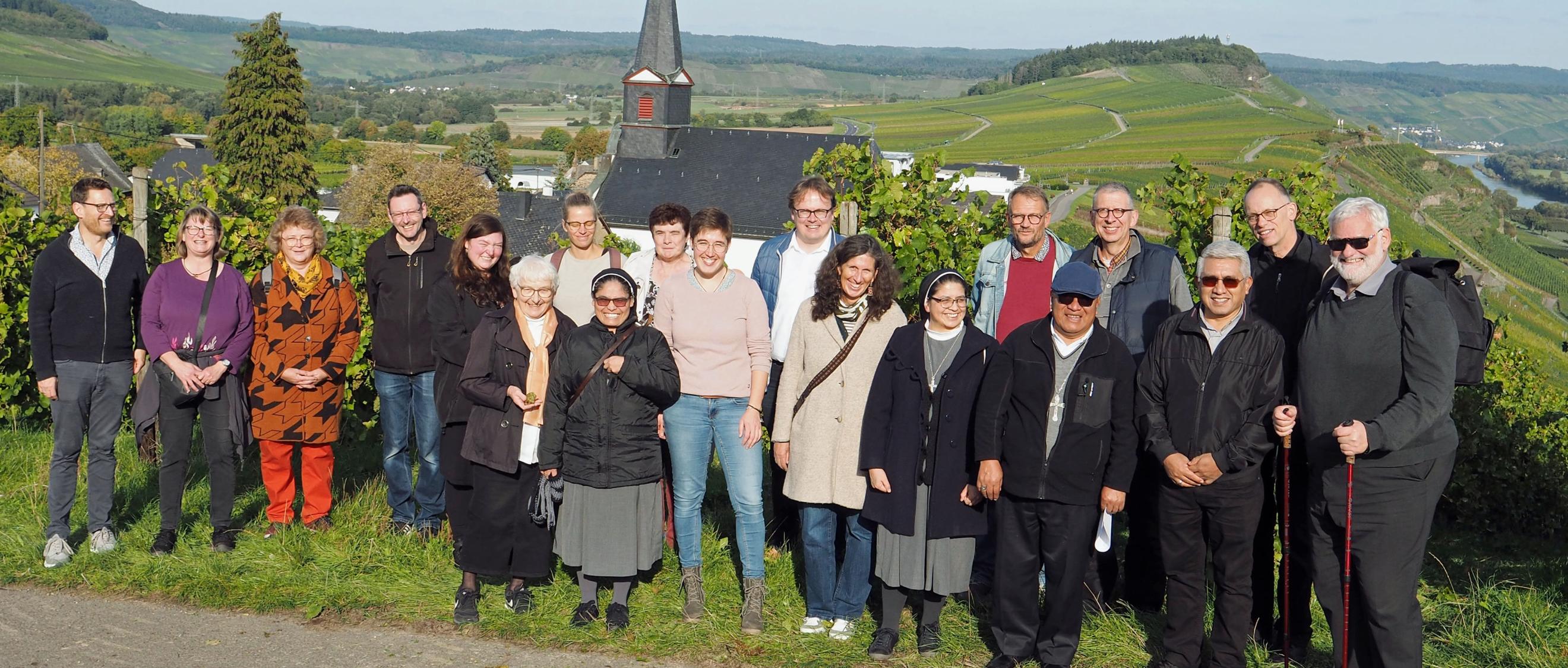 Eine Gruppe Menschen lacht vor einem Panorama mit einer Kirche in die Kamera