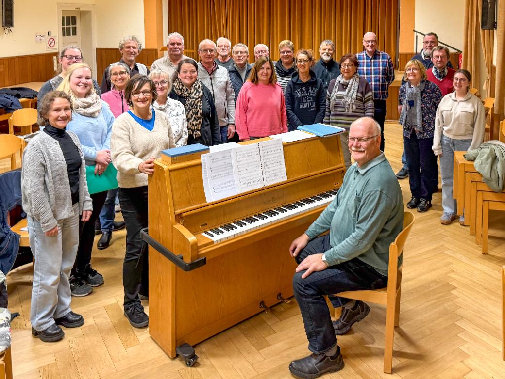 Ein Mann sitzt am Klavier, eine Gruppe Sängerinnen und Sänger steht drumherum
