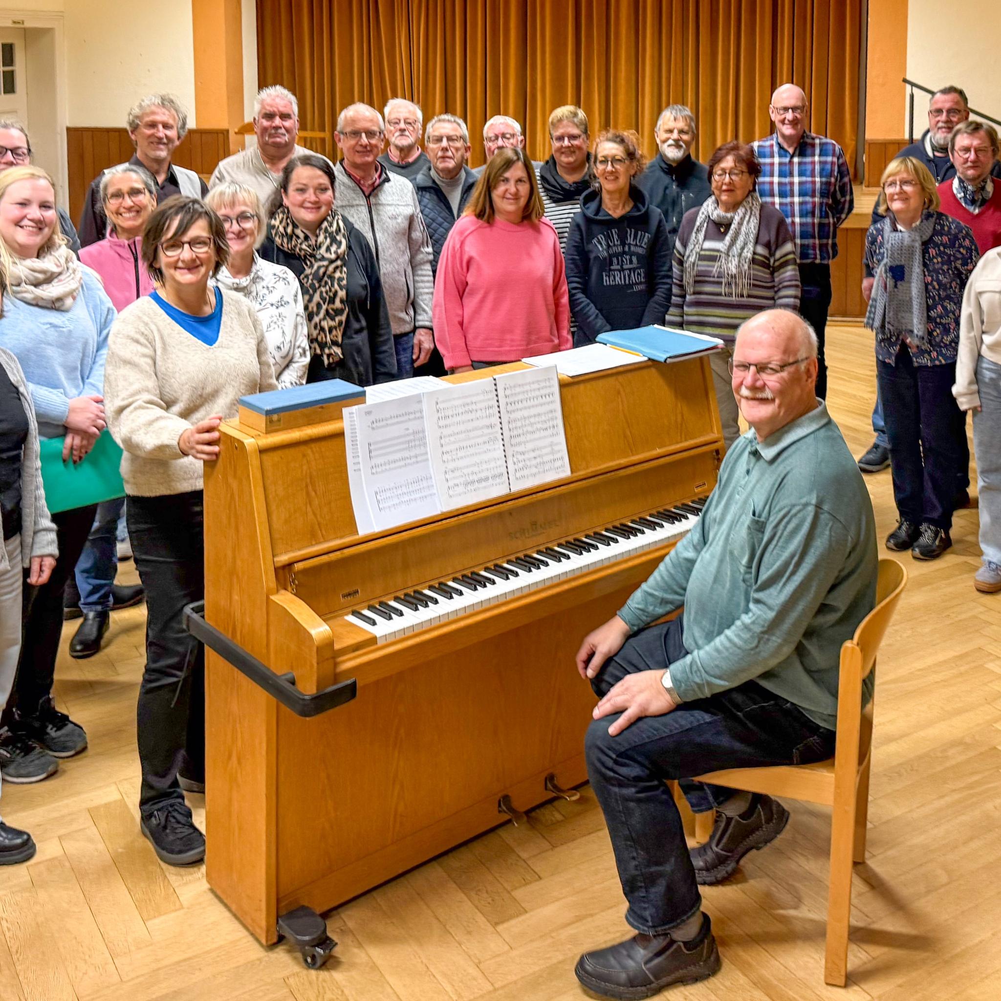 Ein Mann sitzt am Klavier, eine Gruppe Sängerinnen und Sänger steht drumherum