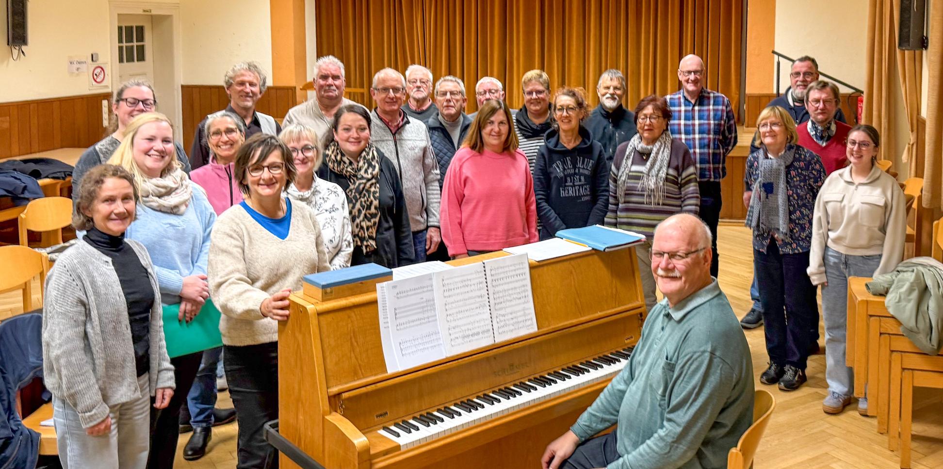 Ein Mann sitzt am Klavier, eine Gruppe Sängerinnen und Sänger steht drumherum