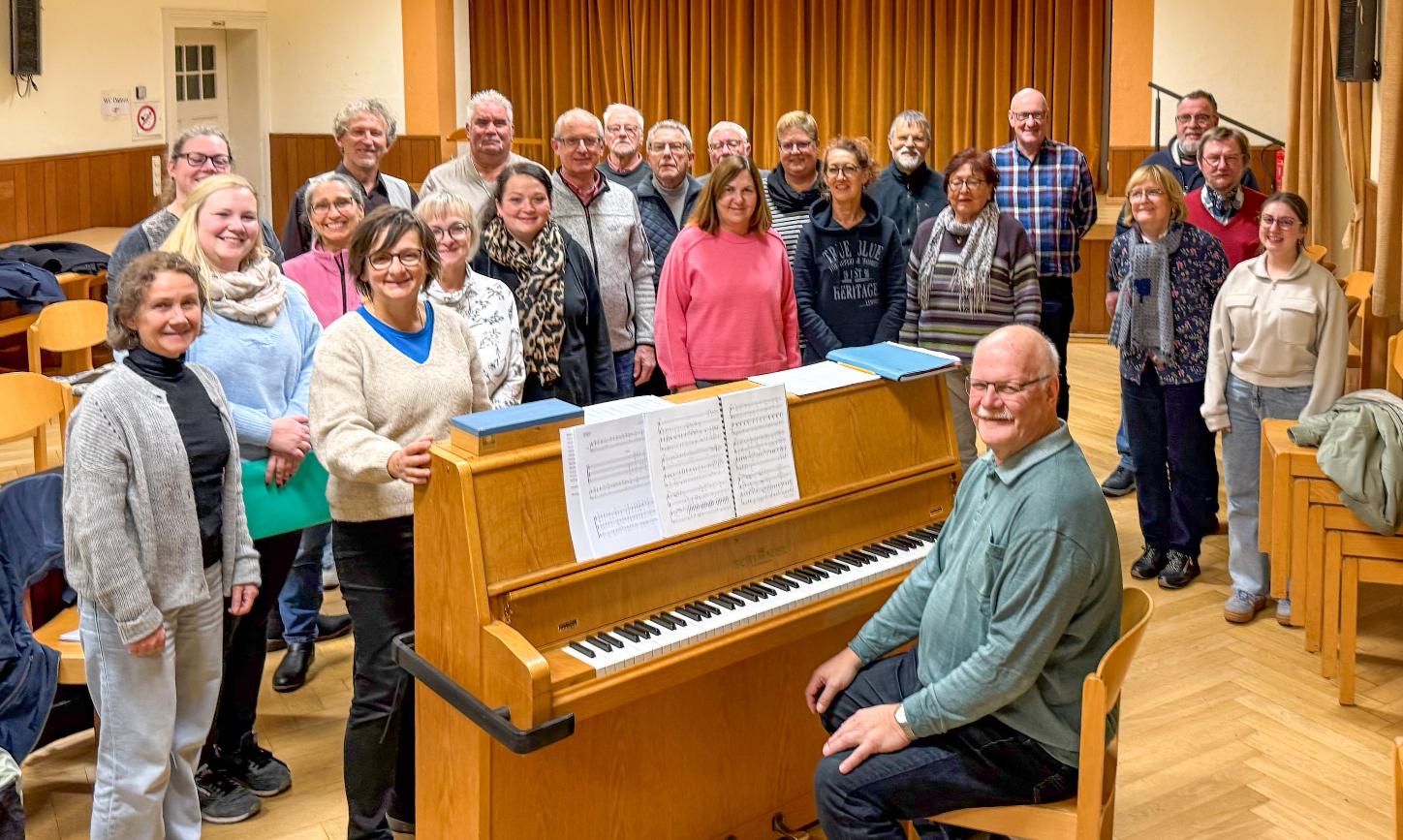 Ein Mann sitzt am Klavier, eine Gruppe Sängerinnen und Sänger steht drumherum
