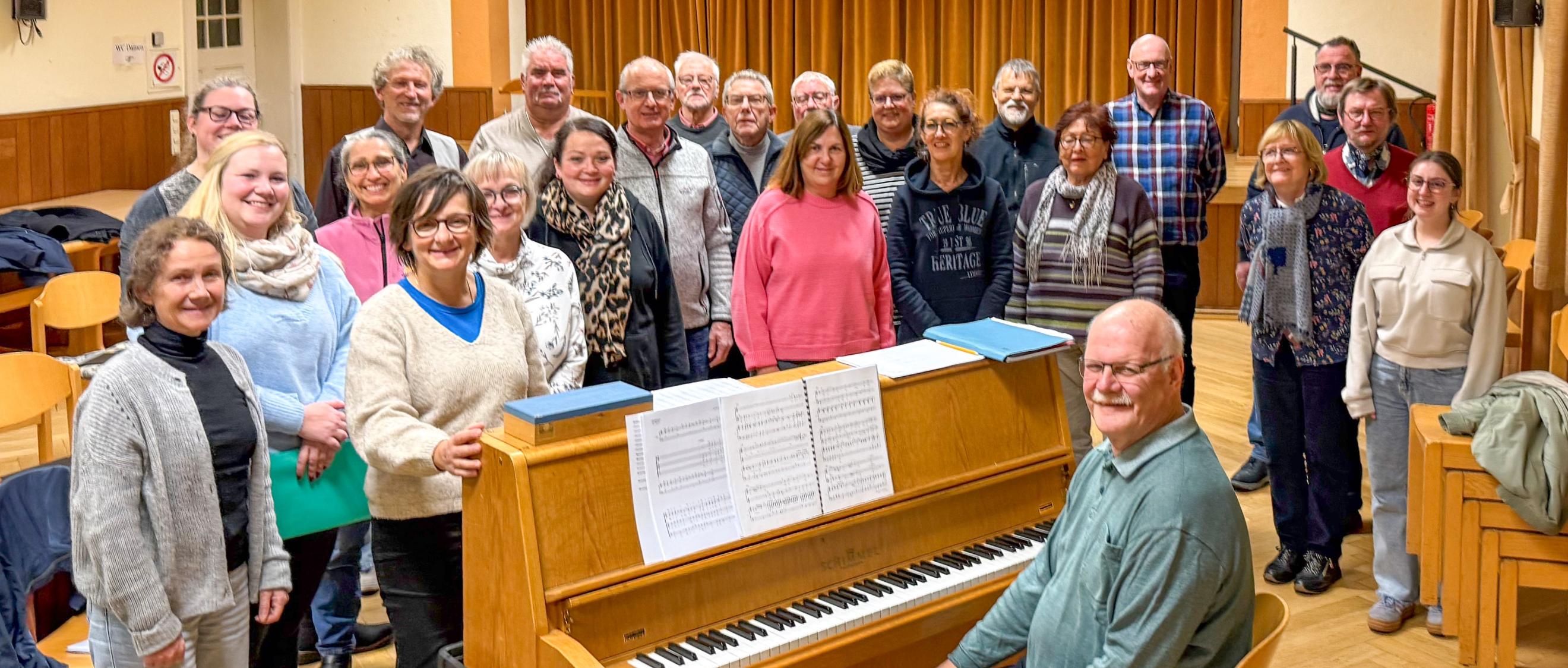 Ein Mann sitzt am Klavier, eine Gruppe Sängerinnen und Sänger steht drumherum