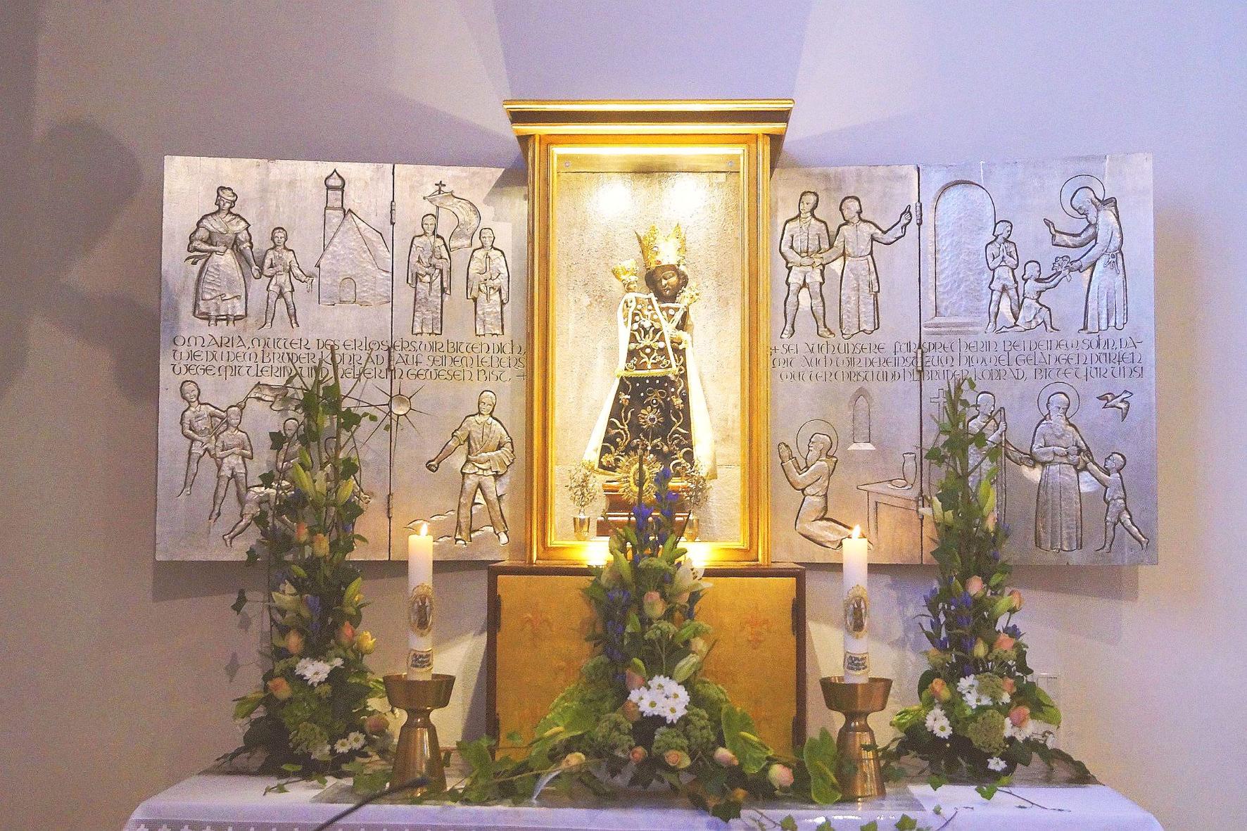 Das Gnadenbild der Schwarzen Madonna steht vor einem Altar mit Szenen aus dem Leben von Bruder Konrad.