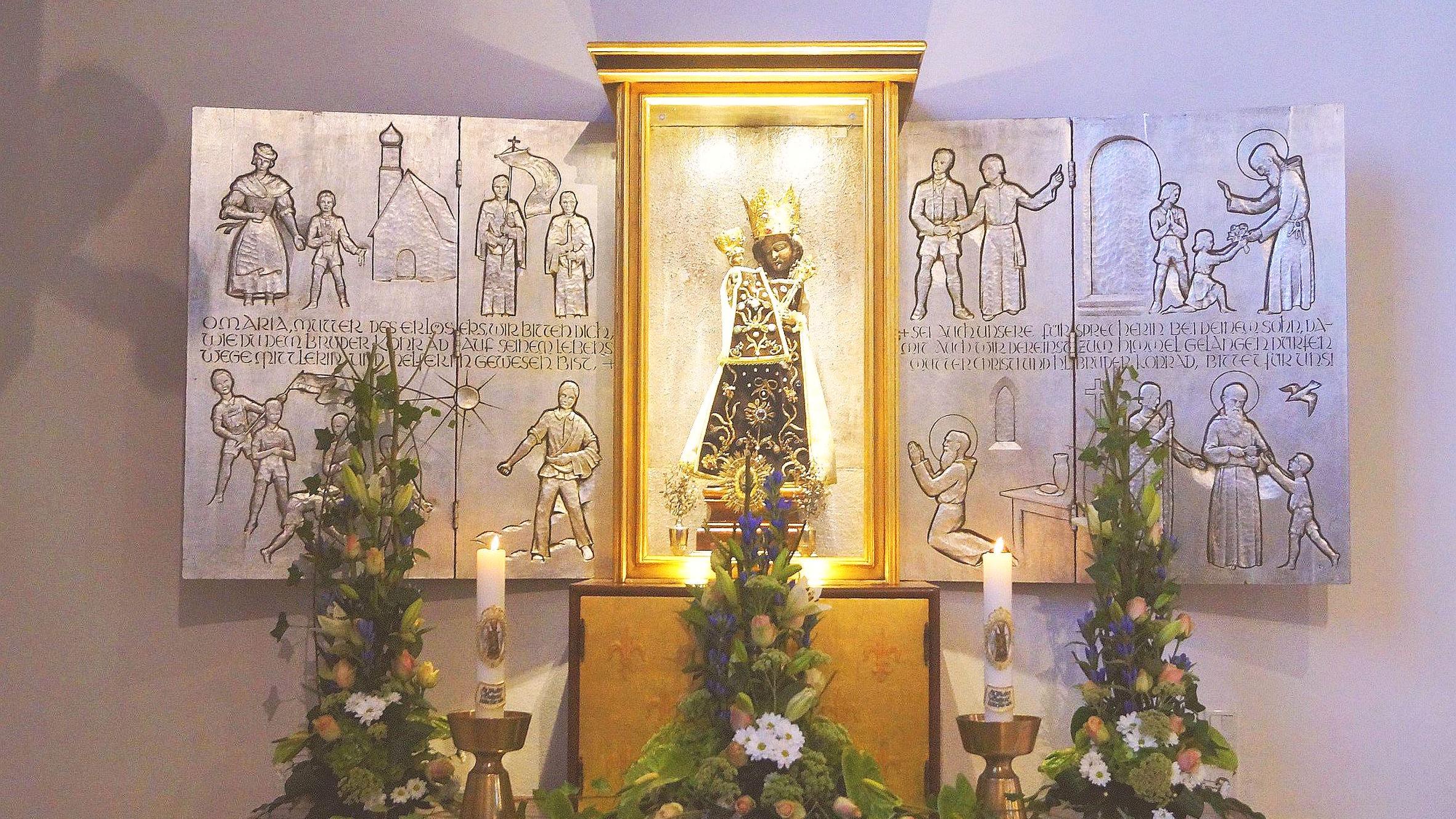 Das Gnadenbild der Schwarzen Madonna steht vor einem Altar mit Szenen aus dem Leben von Bruder Konrad.