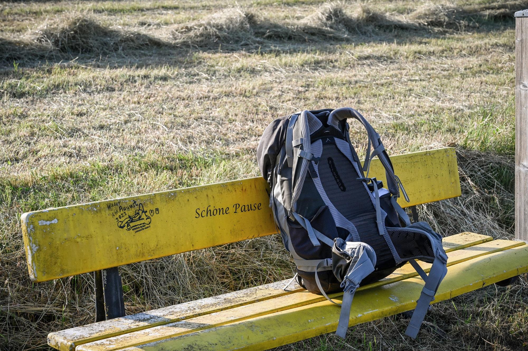 Ein Rucksack steht auf einer gelben Bank vor einer Wiese
