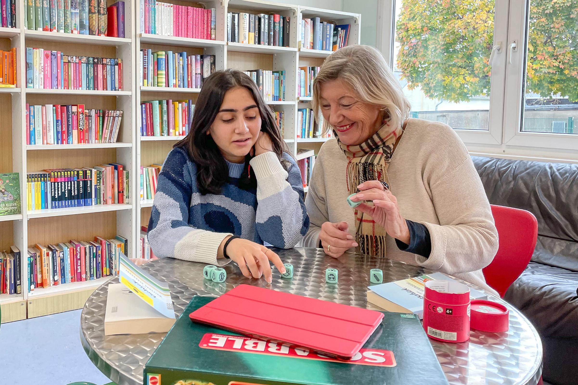 Zwei Frauen spielen in einer Bibliothek gemeinsam ein Würfelspiel.