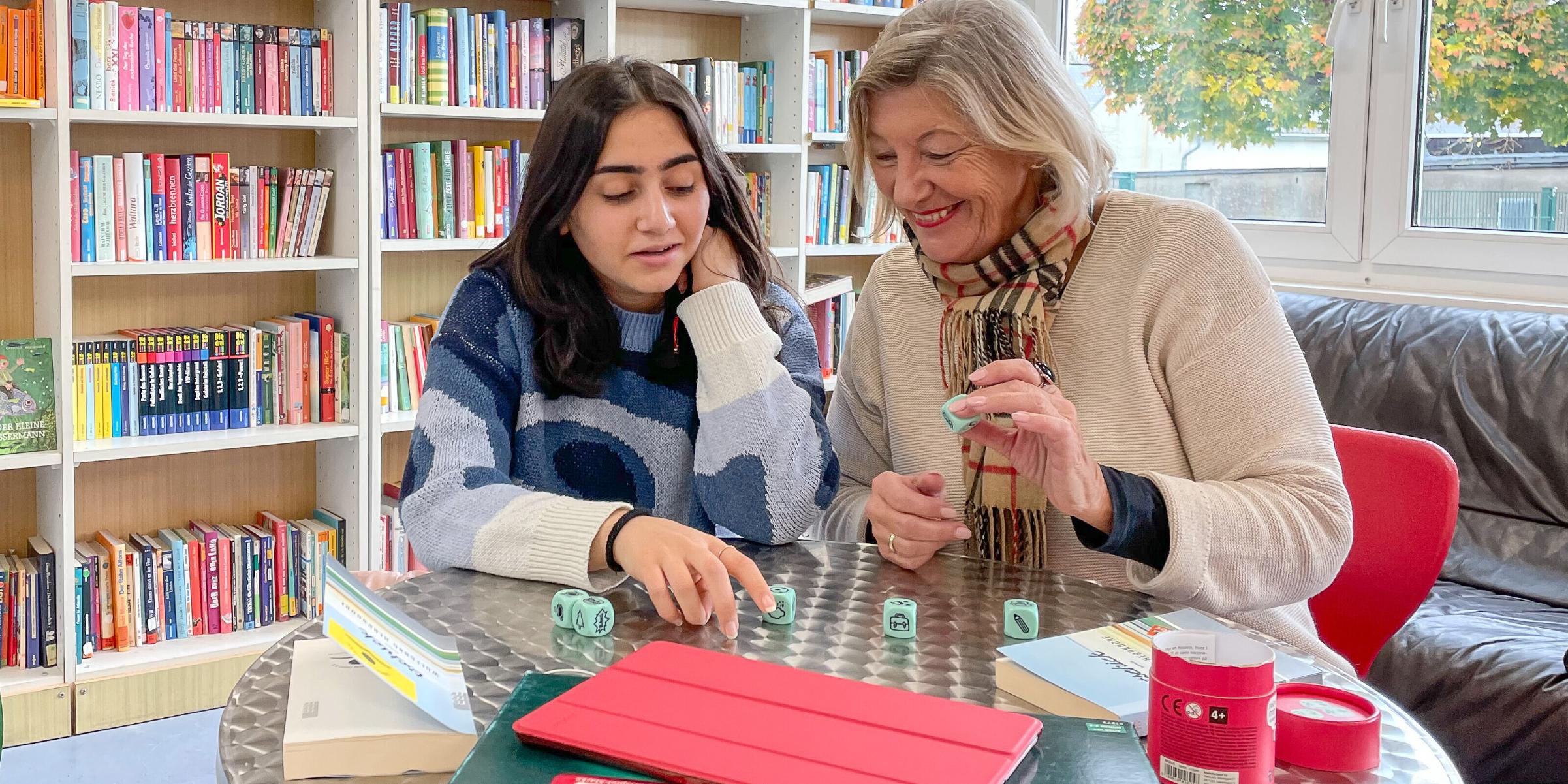 Zwei Frauen spielen in einer Bibliothek gemeinsam ein Würfelspiel.