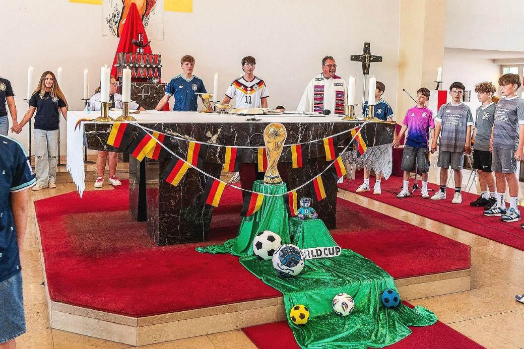 Pfarrer Peter Leick steht gemeinsam mit in Fußball-Dress gekleideten Kindern und Jugendlichen um den passend zur WM geschmückten Altar.