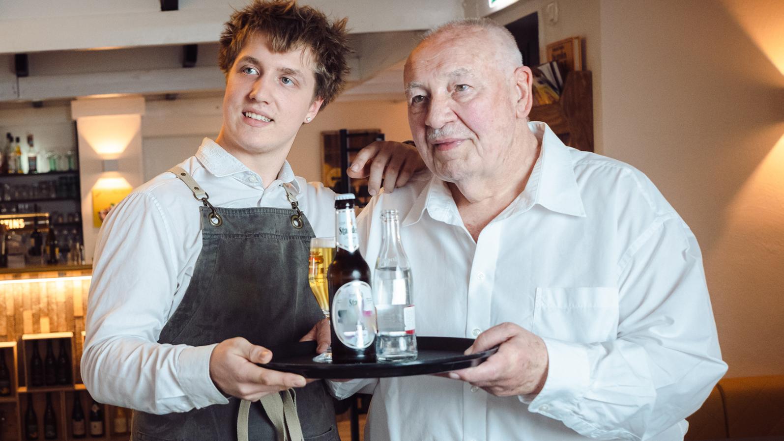 Zwei Männer halten gemeinsam ein Tablet mit Getränken.