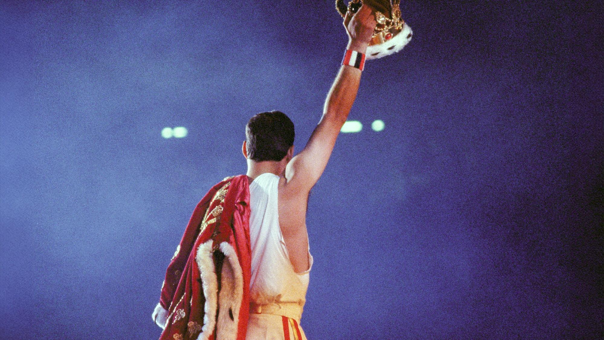 Queen-Sänger Freedy Mercury hält  bei einem Konzert eine Krone in die Höhe.