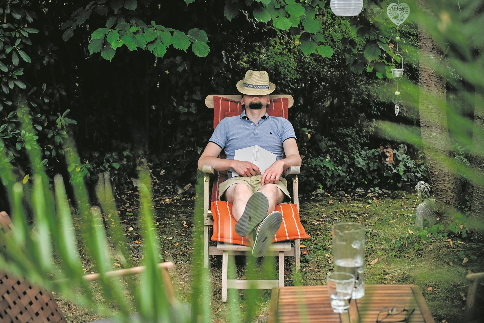 Ein Mann mit einem Hut auf dem Gesicht sitzt in einem Gartenstuhl und schläft, am 26. August 2025 in einem Garten in Bonn. Auf seinem Schoß liegt ein Buch.