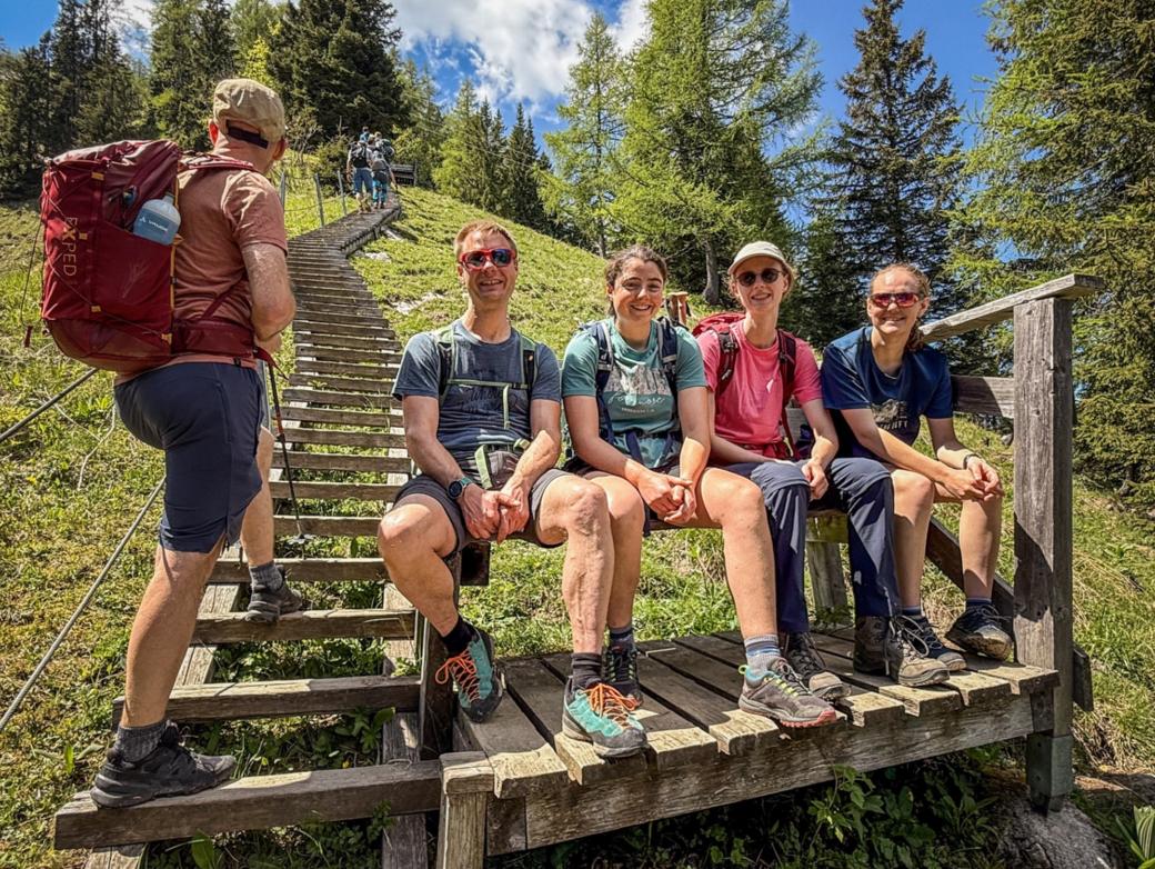Bergsteiger sitzen am Fuß einer Holztreppe auf einer Bank.