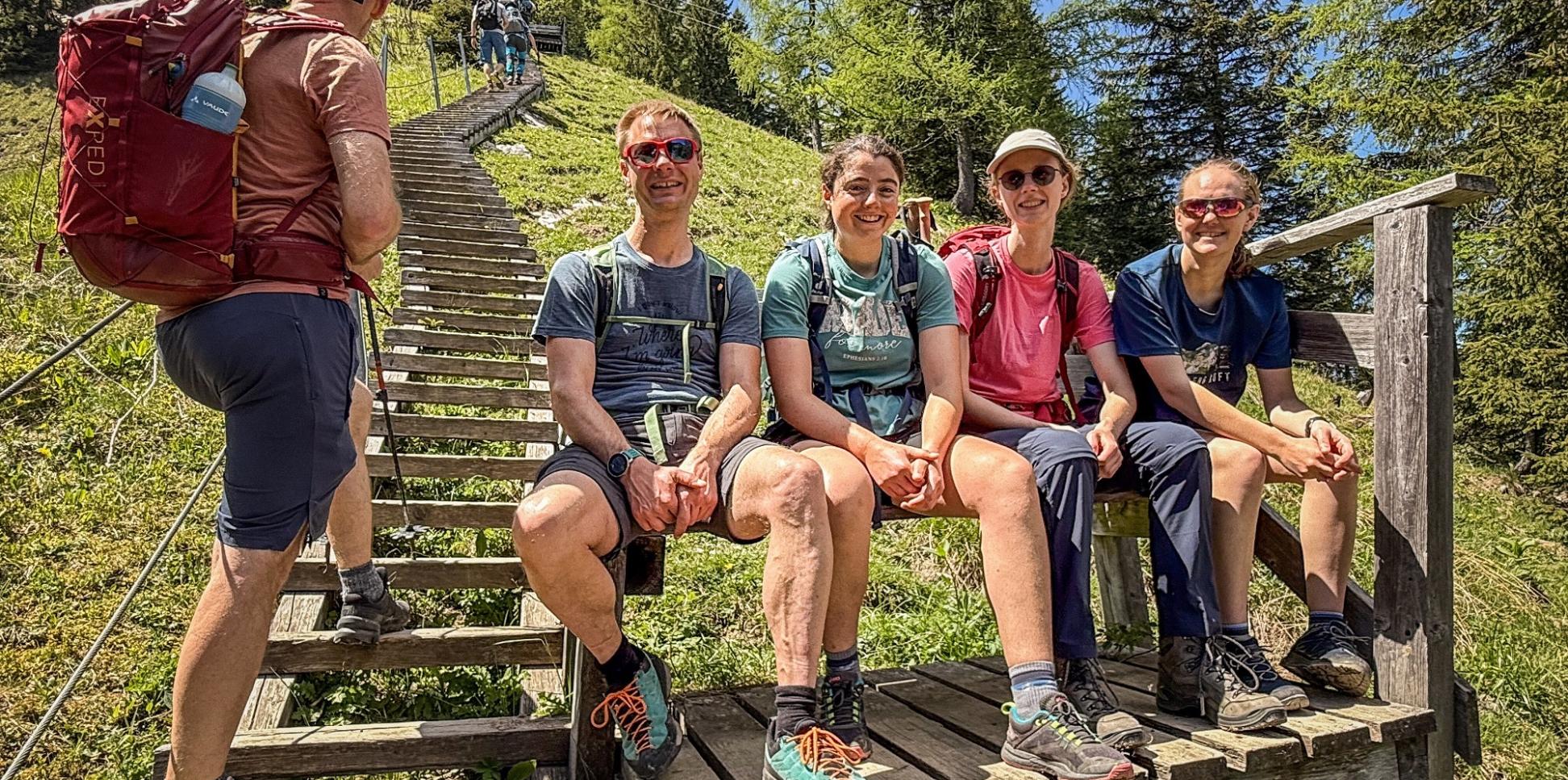 Bergsteiger sitzen am Fuß einer Holztreppe auf einer Bank.