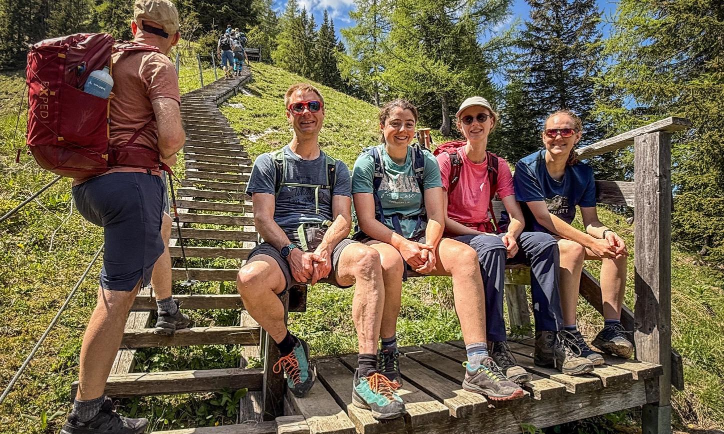 Bergsteiger sitzen am Fuß einer Holztreppe auf einer Bank.