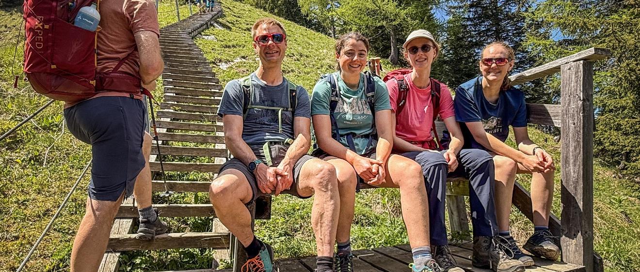 Bergsteiger sitzen am Fuß einer Holztreppe auf einer Bank.