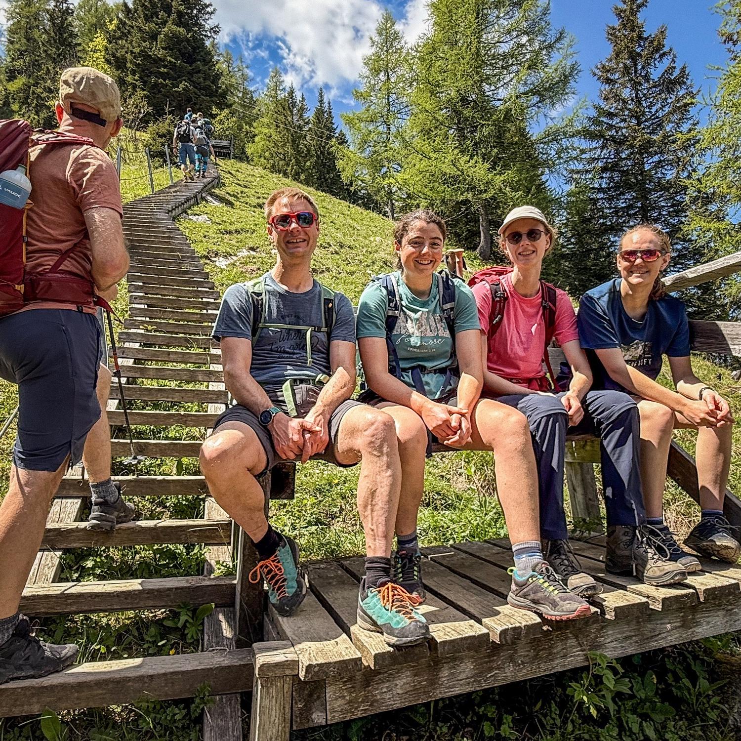Bergsteiger sitzen am Fuß einer Holztreppe auf einer Bank.