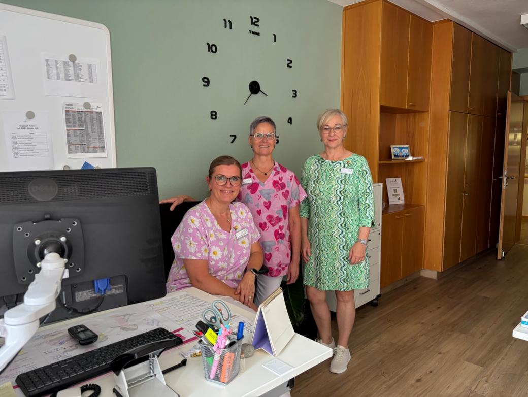Hospizleiterin Barbara Klein (links) und Palliativ-Pflegefachkraft Iris Kirchen sitzen gemeinsam an einem Tisch unter einem Klimagerät.