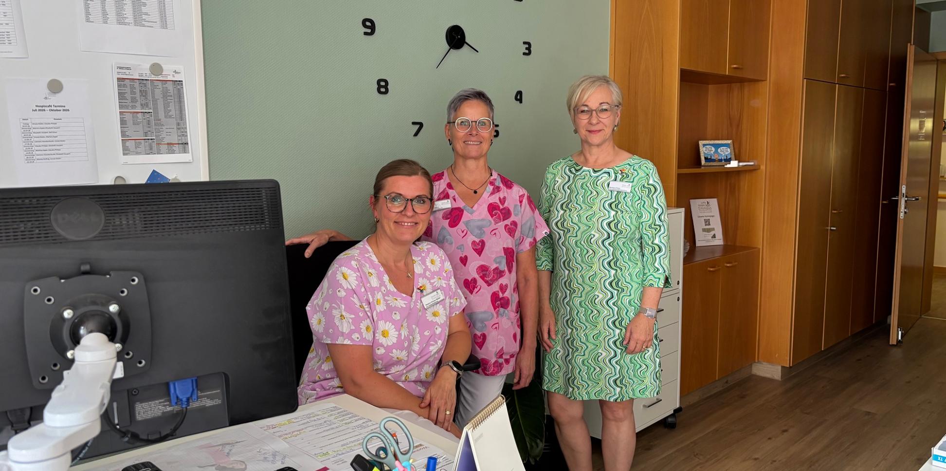 Hospizleiterin Barbara Klein (links) und Palliativ-Pflegefachkraft Iris Kirchen sitzen gemeinsam an einem Tisch unter einem Klimagerät.