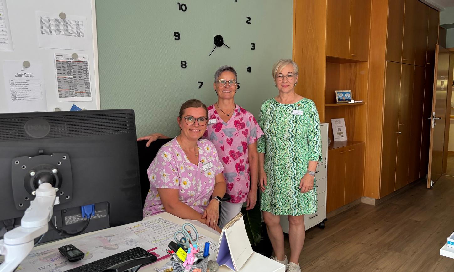 Hospizleiterin Barbara Klein (links) und Palliativ-Pflegefachkraft Iris Kirchen sitzen gemeinsam an einem Tisch unter einem Klimagerät.