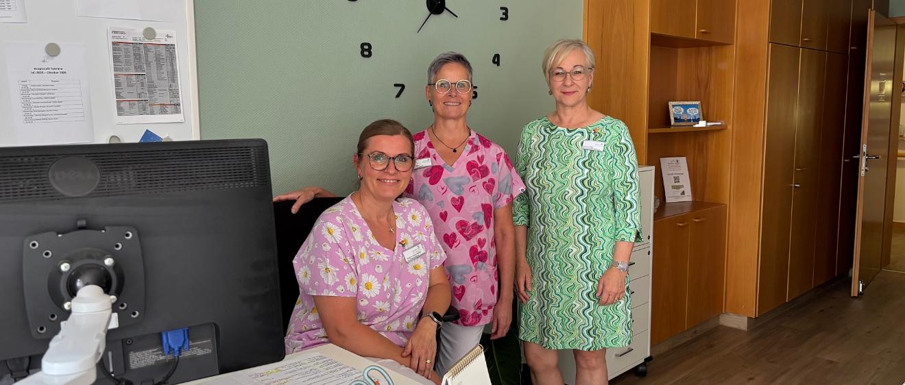 Hospizleiterin Barbara Klein (links) und Palliativ-Pflegefachkraft Iris Kirchen sitzen gemeinsam an einem Tisch unter einem Klimagerät.