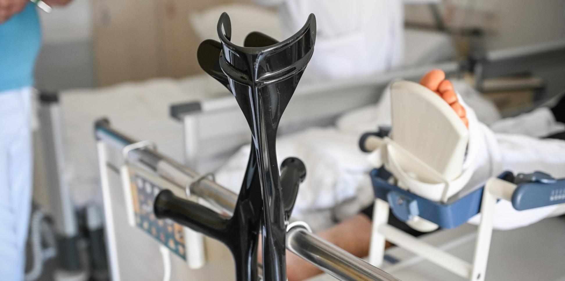 An einem Krankenhausbett lehnt ein Paar Krücken. Von der Person im Bett ist ein verletzter Fuß im Bild.