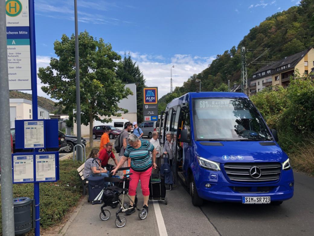 Ein blauer Bus hält und lässt Senioren mit ihrem Einkauf einsteigen.