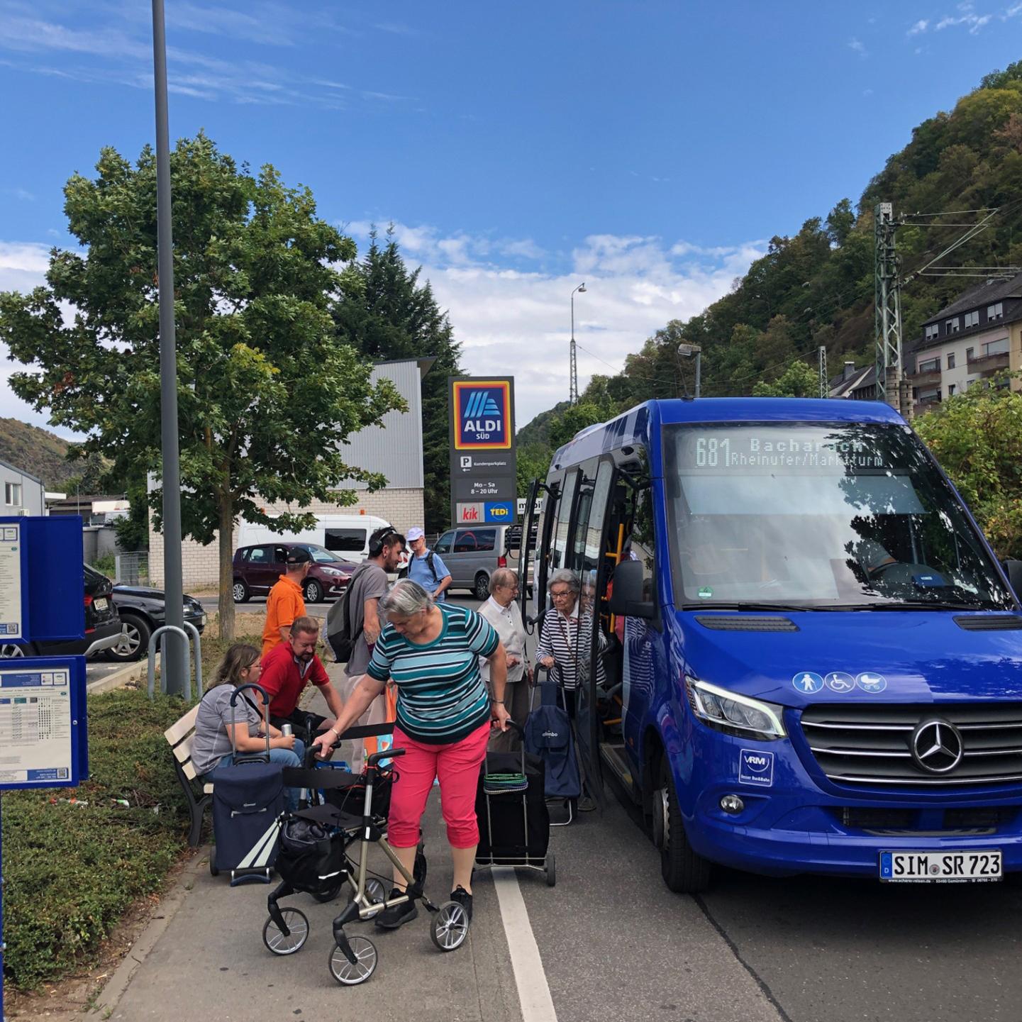 Ein blauer Bus hält und lässt Senioren mit ihrem Einkauf einsteigen.