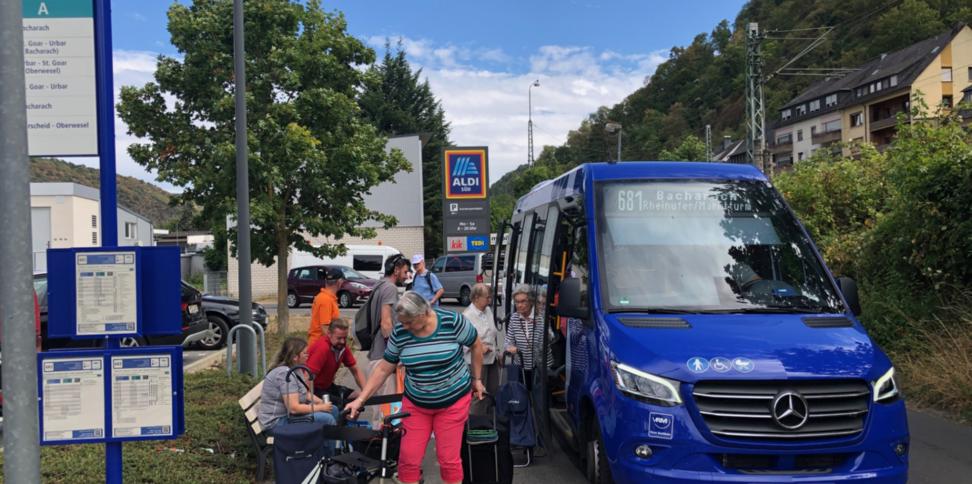 Ein blauer Bus hält und lässt Senioren mit ihrem Einkauf einsteigen.