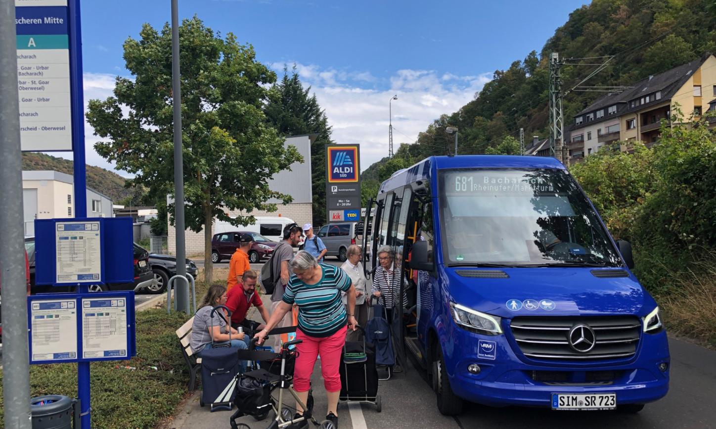 Ein blauer Bus hält und lässt Senioren mit ihrem Einkauf einsteigen.