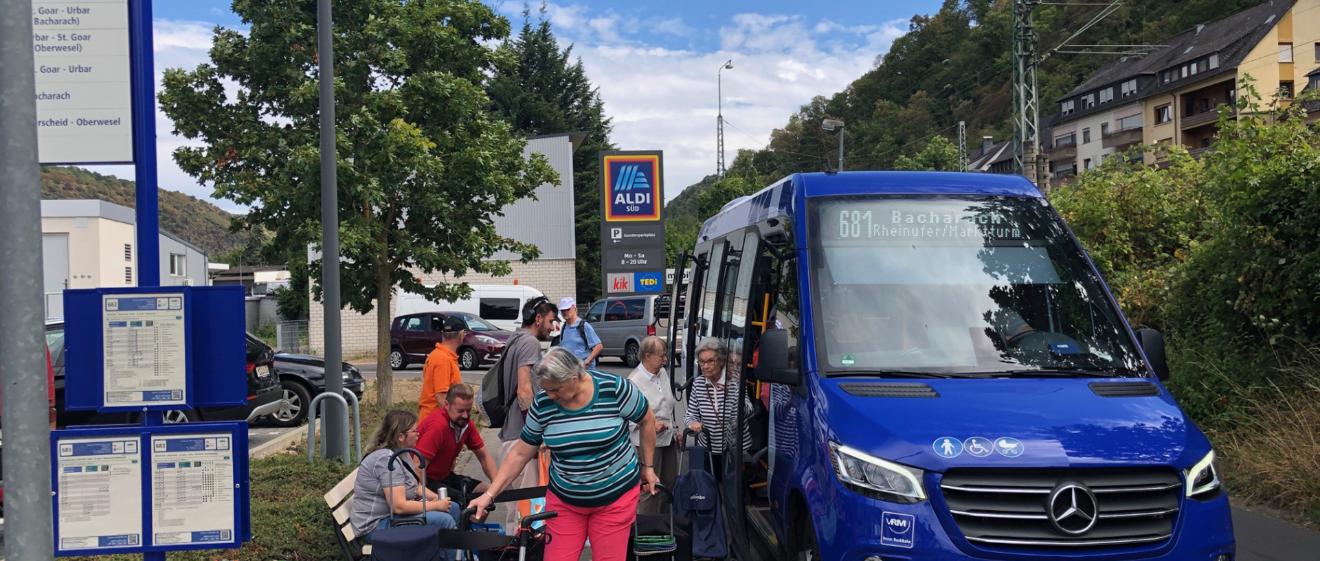 Ein blauer Bus hält und lässt Senioren mit ihrem Einkauf einsteigen.