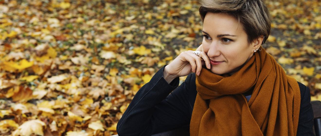 Eine Frau sitzt auf einer Bank und schaut nachdenklich.