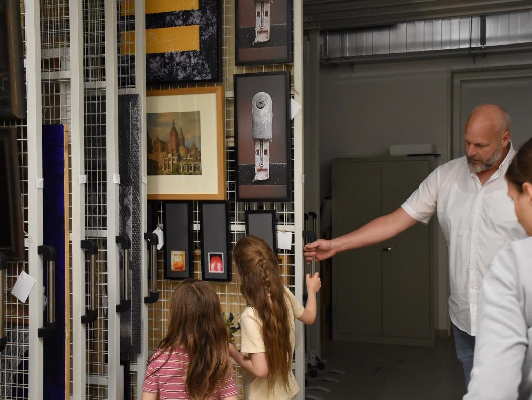 Museumsdirektor von Ahn zeigt zwei Kindern Bilder in einem Tresorschrank.