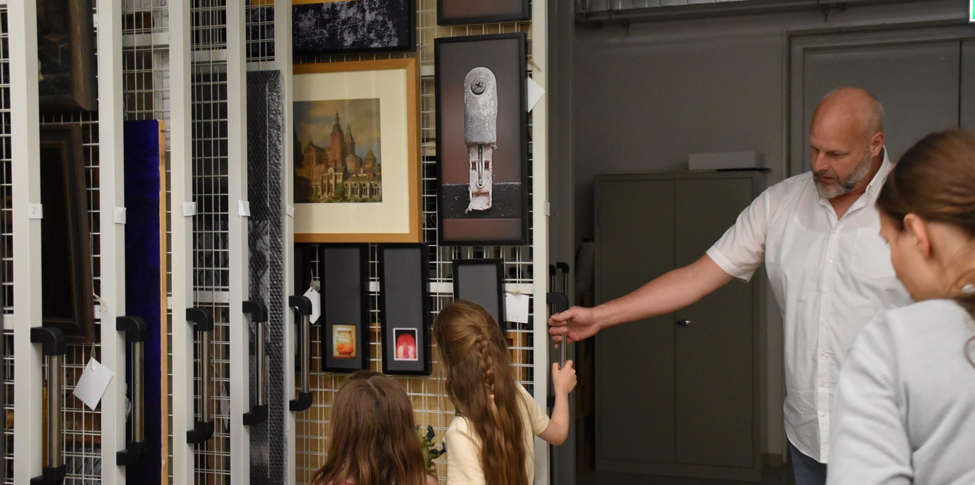 Museumsdirektor von Ahn zeigt zwei Kindern Bilder in einem Tresorschrank.