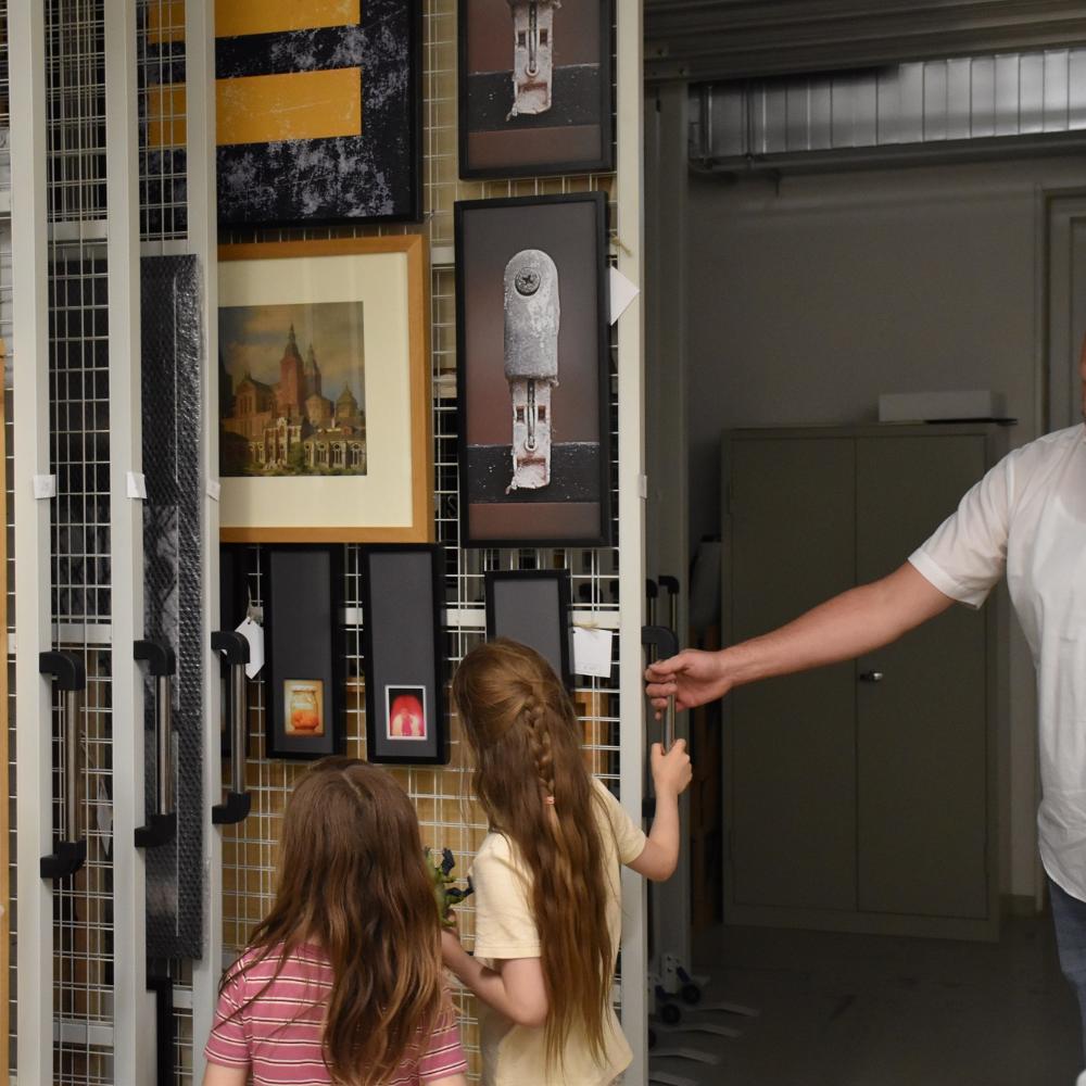 Museumsdirektor von Ahn zeigt zwei Kindern Bilder in einem Tresorschrank.
