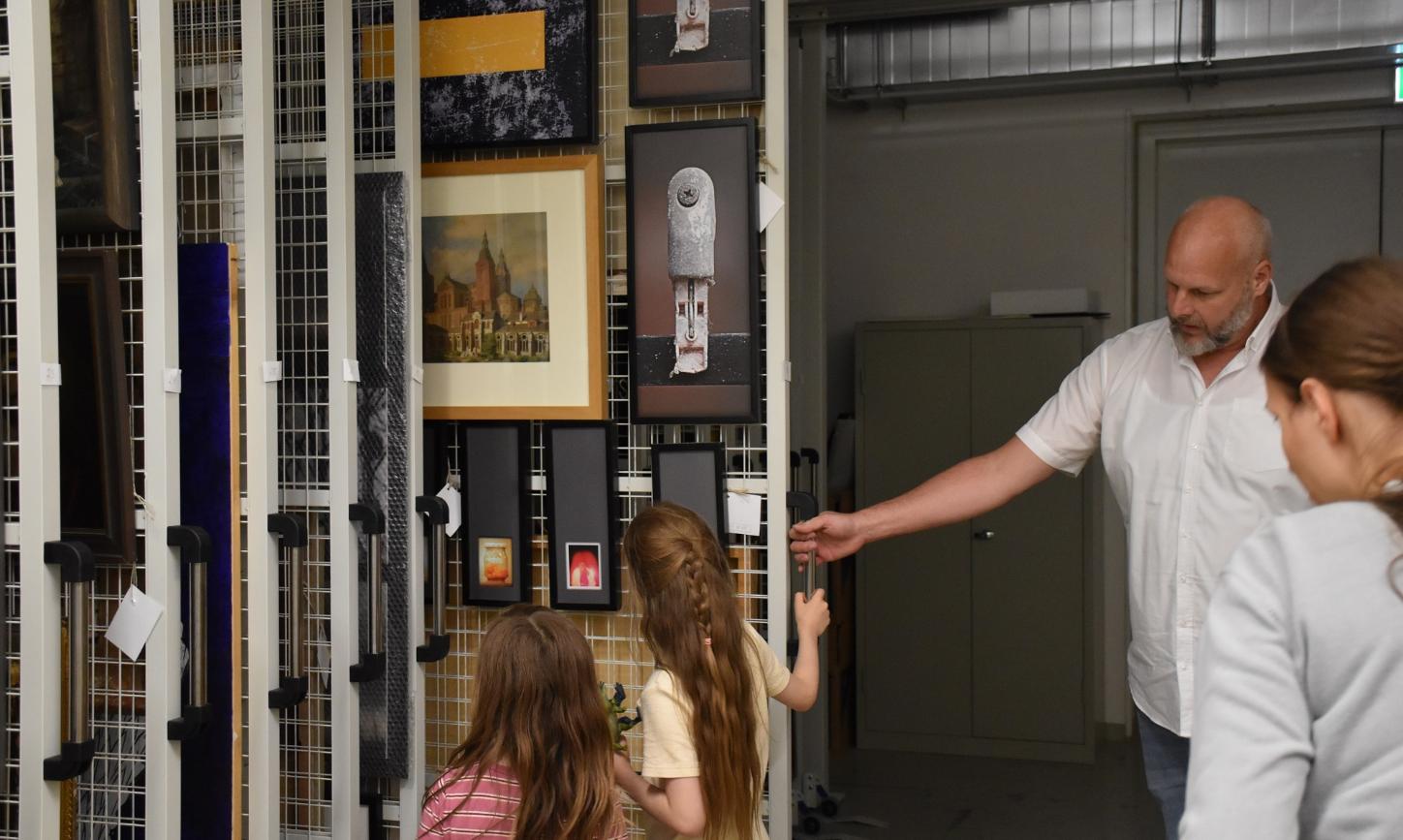 Museumsdirektor von Ahn zeigt zwei Kindern Bilder in einem Tresorschrank.