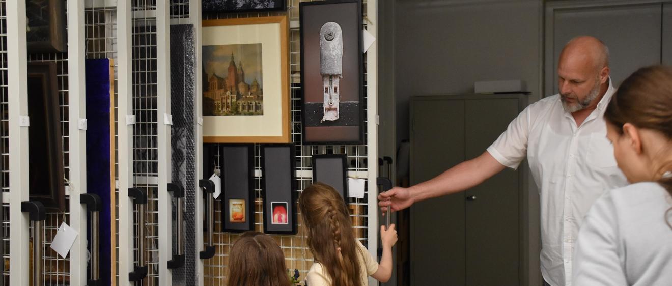 Museumsdirektor von Ahn zeigt zwei Kindern Bilder in einem Tresorschrank.