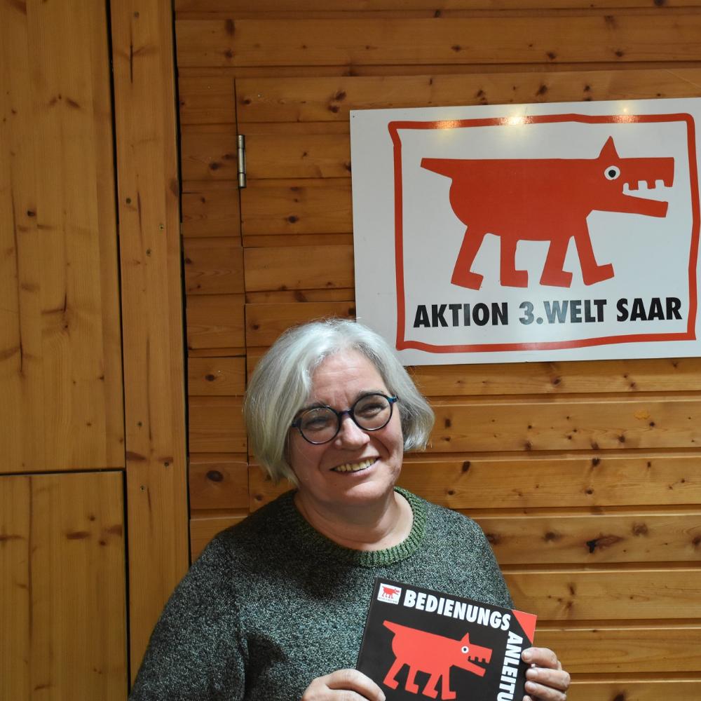 Portraitbild von Gertrud Selzer. In den Händen hält sie ein Plakat der Aktion 3. Welt Saar.