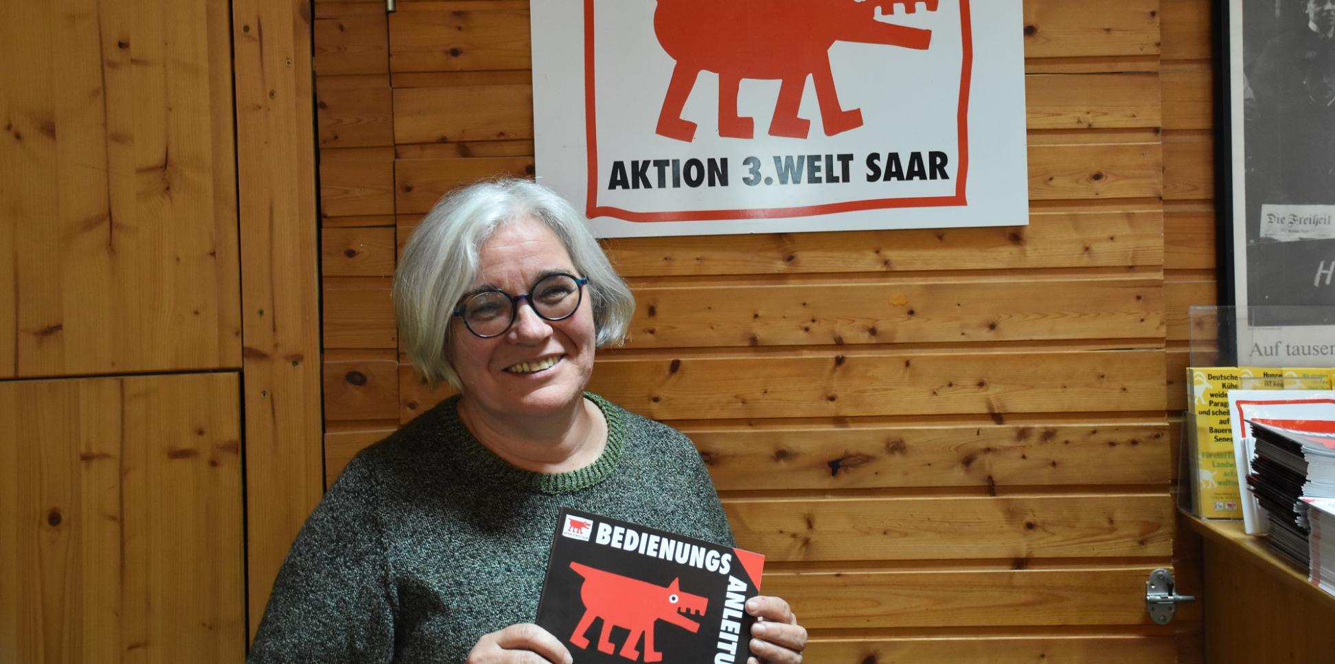 Portraitbild von Gertrud Selzer. In den Händen hält sie ein Plakat der Aktion 3. Welt Saar.