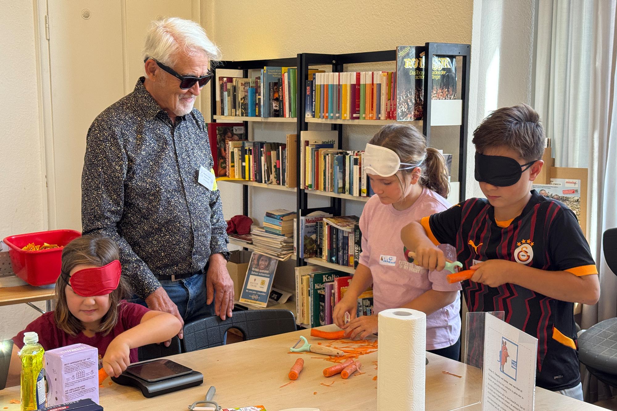 Peter Berweiler, selbst fast blind, zeigt Kindern beim „Maus-Türöffnertag“, wie das Gemüseschälen mit verbundenen Augen funktionieren kann.