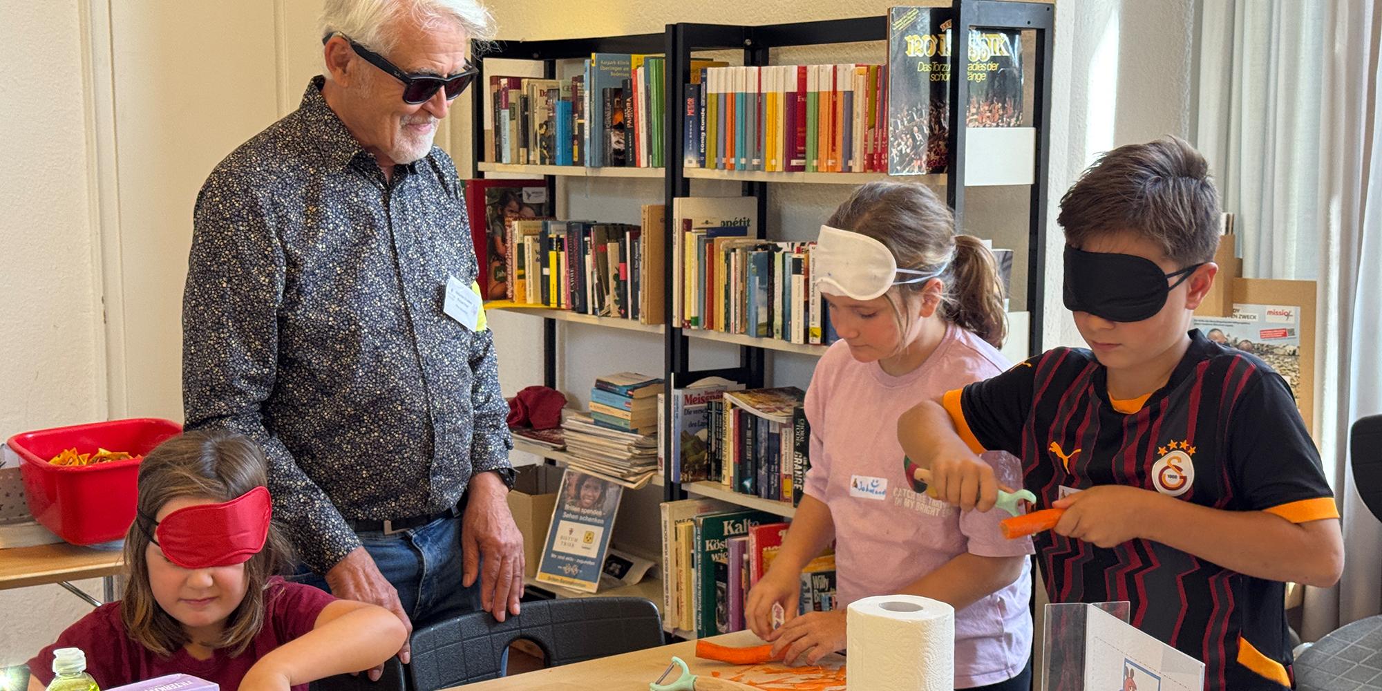 Peter Berweiler, selbst fast blind, zeigt Kindern beim „Maus-Türöffnertag“, wie das Gemüseschälen mit verbundenen Augen funktionieren kann. (c) Christina Libeaux Peter Berweiler, selbst fast blind, zeigt Kindern beim „Maus-Türöffnertag“, wie das Gemüseschälen mit verbundenen Augen funktionieren kann.