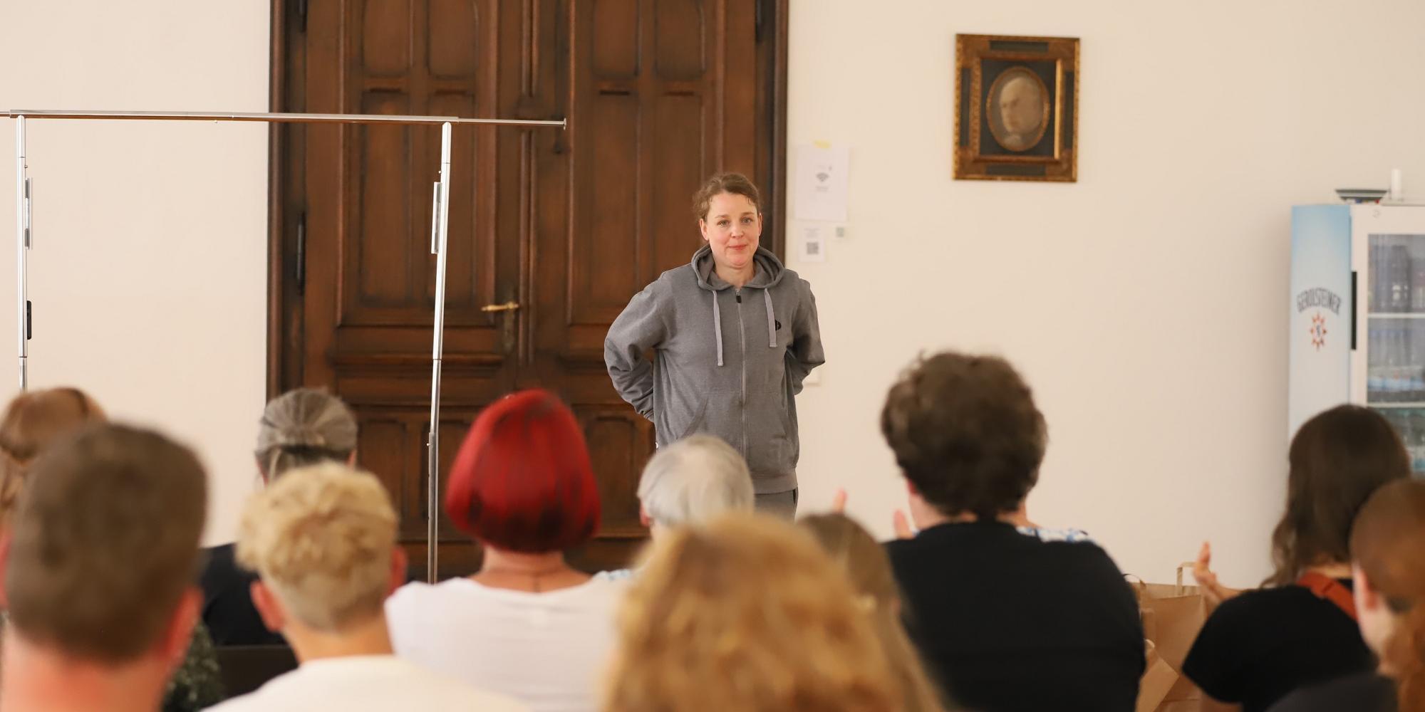 Schauspielerin Anna Bernstein steht, Hände in den Taschen, gekleidet in einen grauen Hoodie, vor dem Publikum. (c) Luca Peranni/Bistum Trier Schauspielerin Anna Bernstein steht, Hände in den Taschen, gekleidet in einen grauen Hoodie, vor dem Publikum.