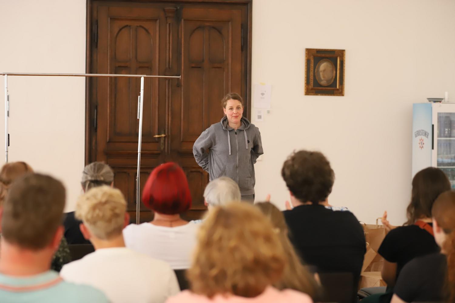 Schauspielerin Anna Bernstein steht, Hände in den Taschen, gekleidet in einen grauen Hoodie, vor dem Publikum.