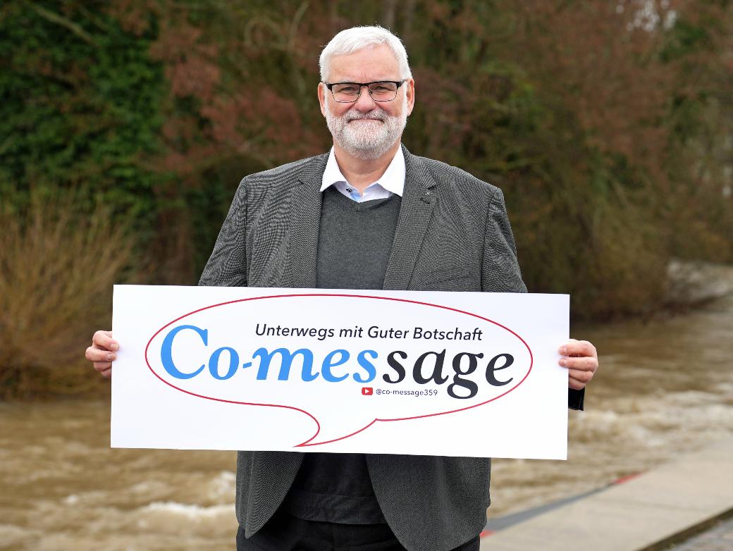 Ein Mann blickt in die Kamera. In den Händen hält er ein Plakat mit der Aufschrift 'Co-message'