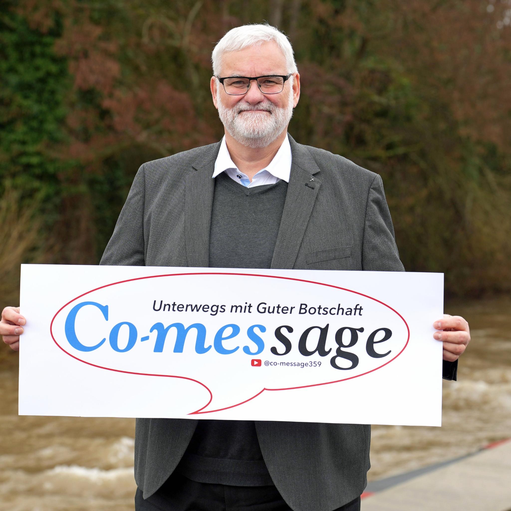 Ein Mann blickt in die Kamera. In den Händen hält er ein Plakat mit der Aufschrift 'Co-message'