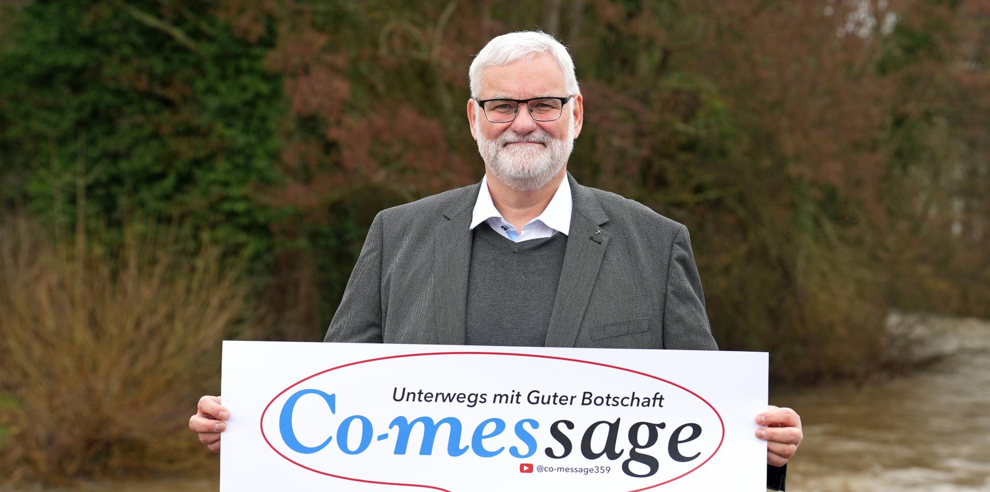 Ein Mann blickt in die Kamera. In den Händen hält er ein Plakat mit der Aufschrift 'Co-message'