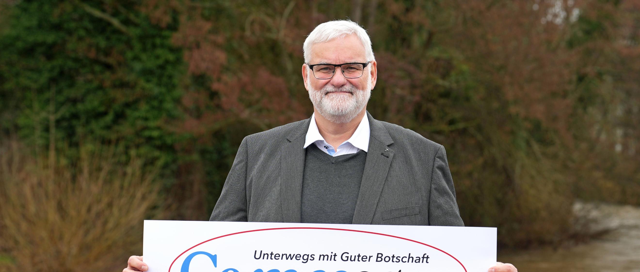 Ein Mann blickt in die Kamera. In den Händen hält er ein Plakat mit der Aufschrift 'Co-message'